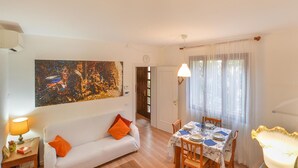 A dining area with a table set for four, a white sofa with orange cushions, and a large abstract painting on the wall.
