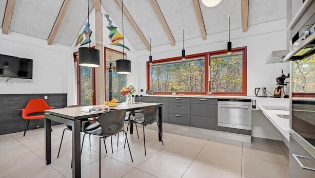 A modern kitchen with a dining area, large windows, and a high ceiling.