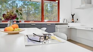 A modern kitchen with a white countertop, a bowl of fruit, and a magazine with glasses on it.