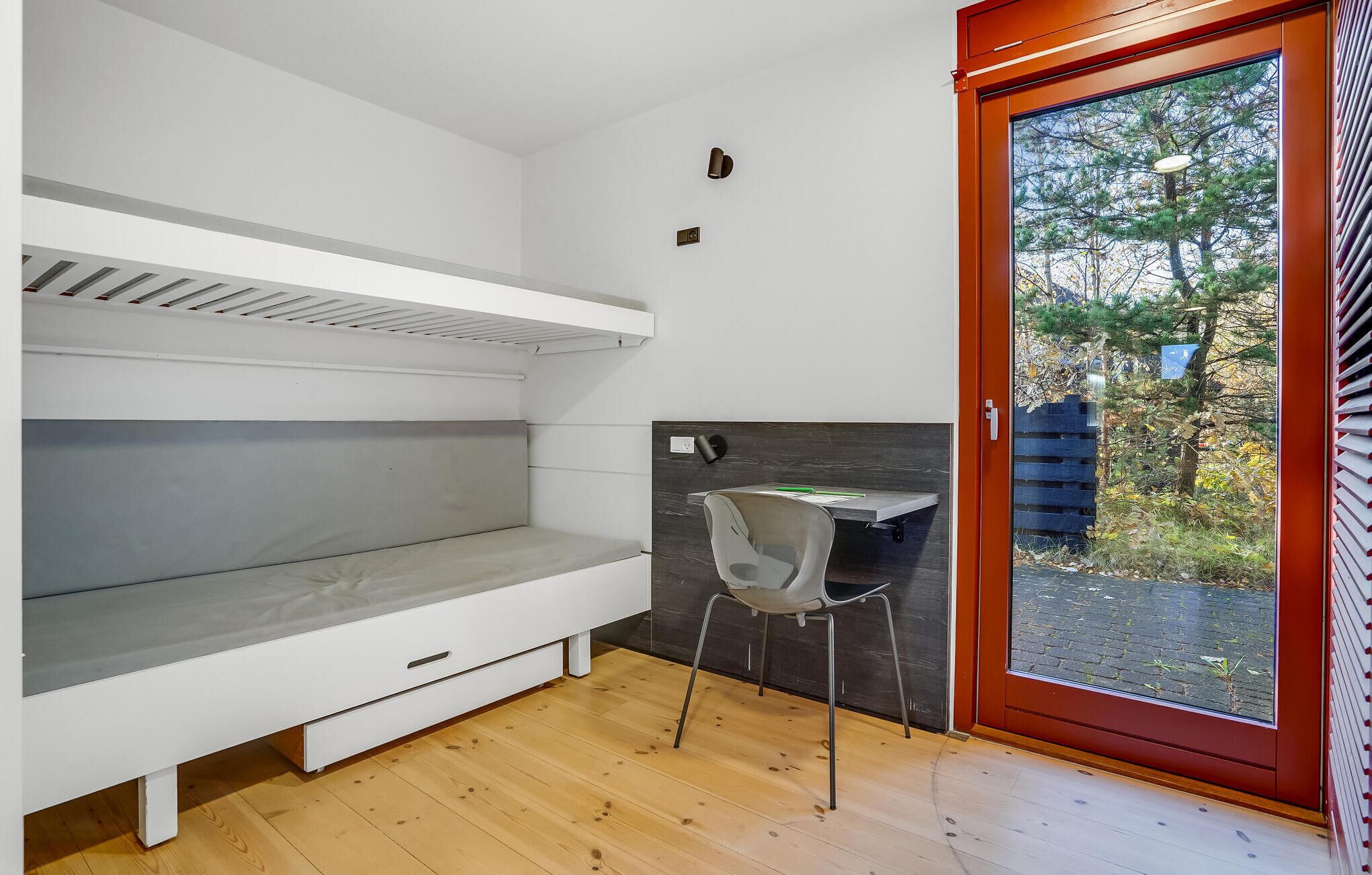 A compact room with a bunk bed, a desk with a chair, and a sliding glass door leading to an outdoor area.