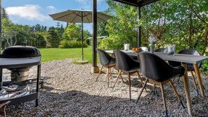 Une terrasse extérieure équipée d’un barbecue, d’une table, de chaises et d’un espace abrité avec un parasol.