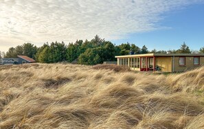 Ein Haus mit überdachter Veranda, umgeben von hohem Gras und Bäumen.