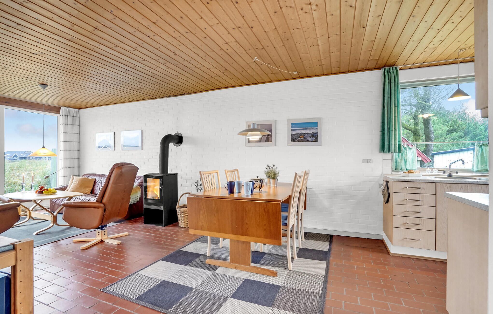 Una habitación acogedora con techo de madera, una mesa de comedor con sillas, estufa empotrada y zona de cocina con lavamanos y armarios.