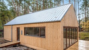 A wooden cabin with a sloped metal roof, large windows, and a wooden deck. - Nice home in Nexø with WiFi (Nexø)