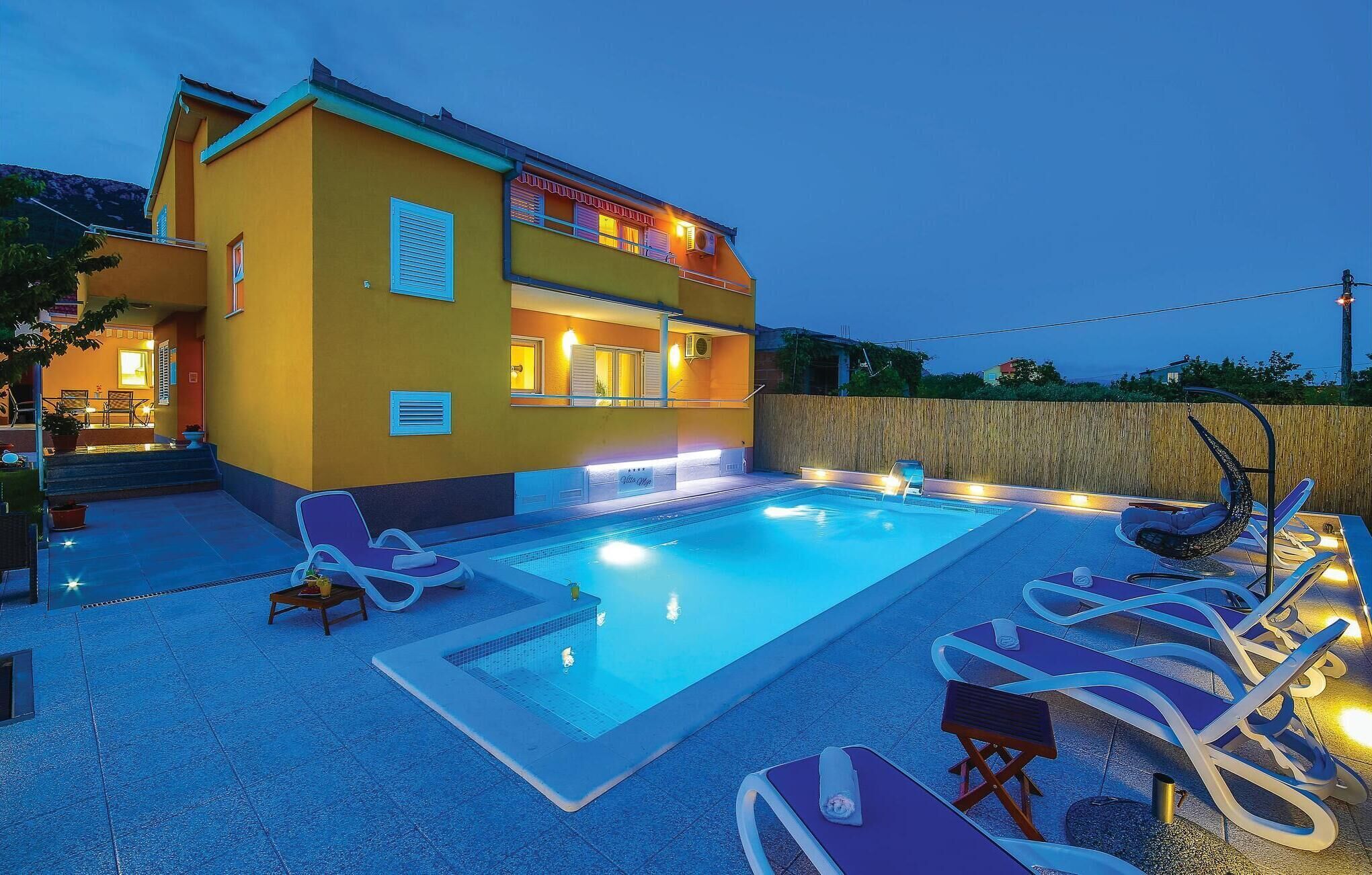 A two-story building with a swimming pool, outdoor seating, and a wooden fence.