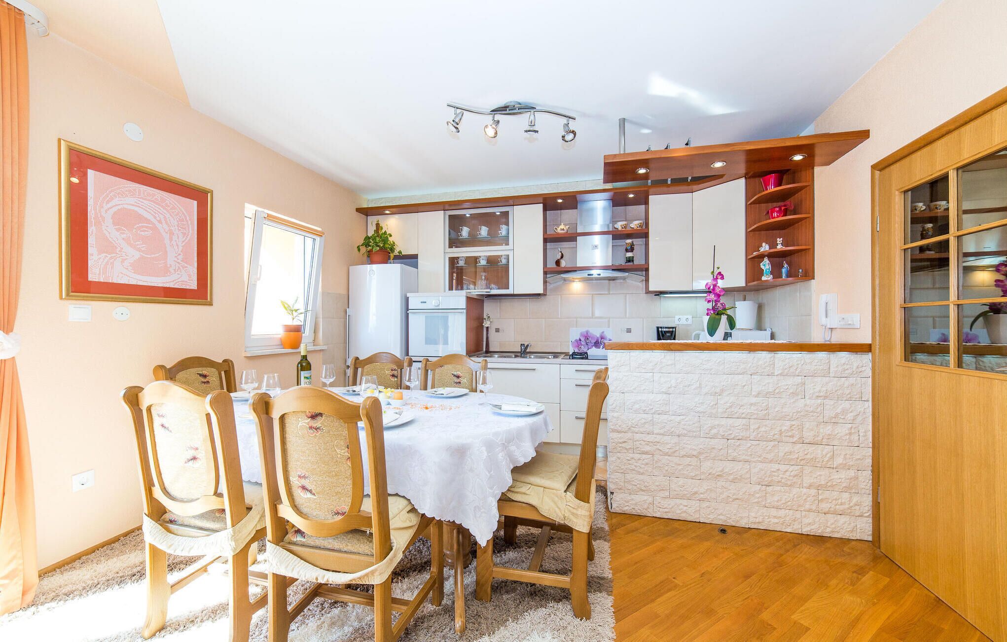 Een gezellige keuken met witte kasten, een eettafel met stoelen, en een klein aanrecht met een spoelbak.