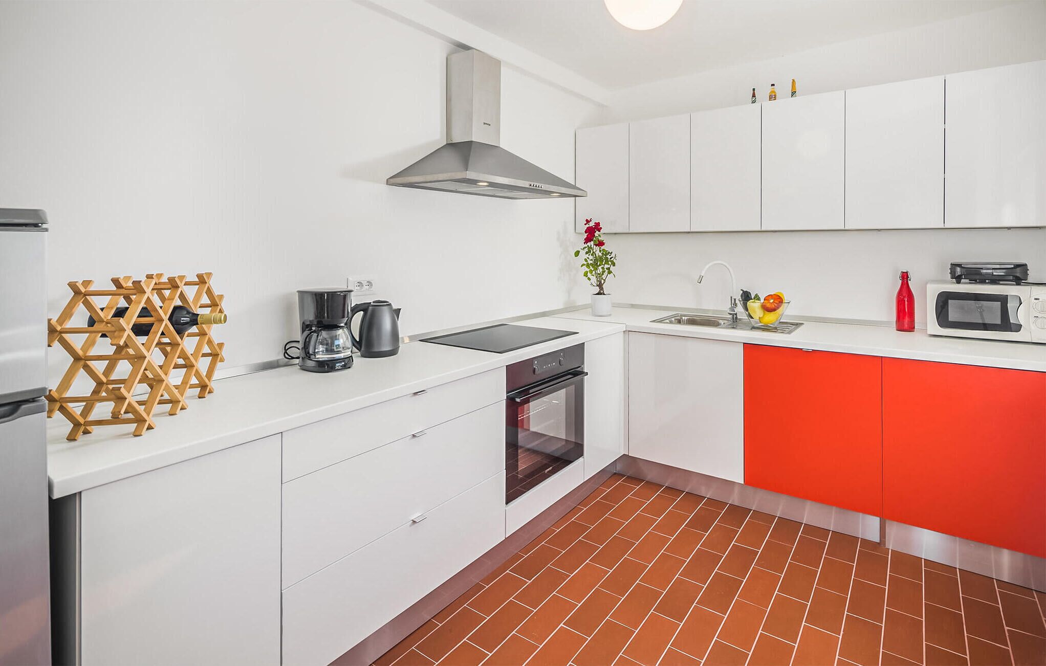 A modern kitchen with white cabinets, a red accent wall, a built-in oven, a coffee maker, and a wine rack.