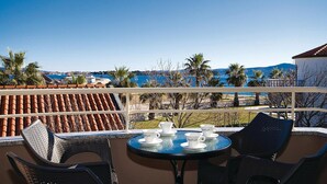 Une terrasse avec une table dressée pour quatre personnes, donnant sur une zone côtière bordée de palmiers et offrant une vue sur la mer.