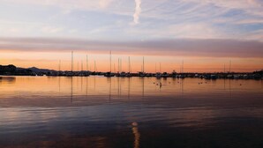 Un port de plaisance où sont amarrés de nombreux voiliers, l’eau est calme et le ciel se pare des couleurs du coucher de soleil.