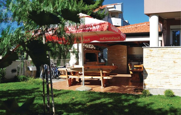 An outdoor dining area with a wooden table and benches, a red umbrella, and a brick wall.