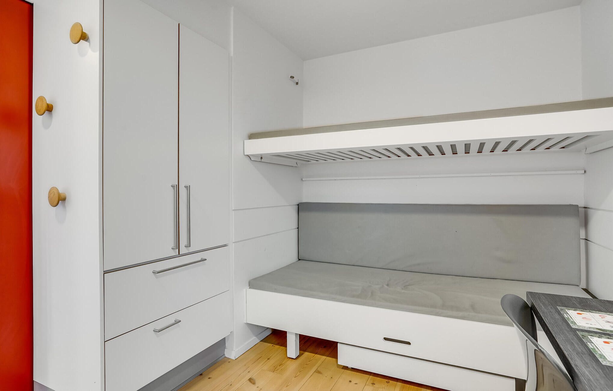 Habitació petita amb una llitera, un armari blanc amb nombrosos tiradors platejats i un escriptori petit amb una cadira.