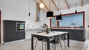 A modern kitchen with a dining area, featuring a large window, a built-in oven, and a central island with chairs. - Cozy home in Grenaa with kitchen (Grenaa)
