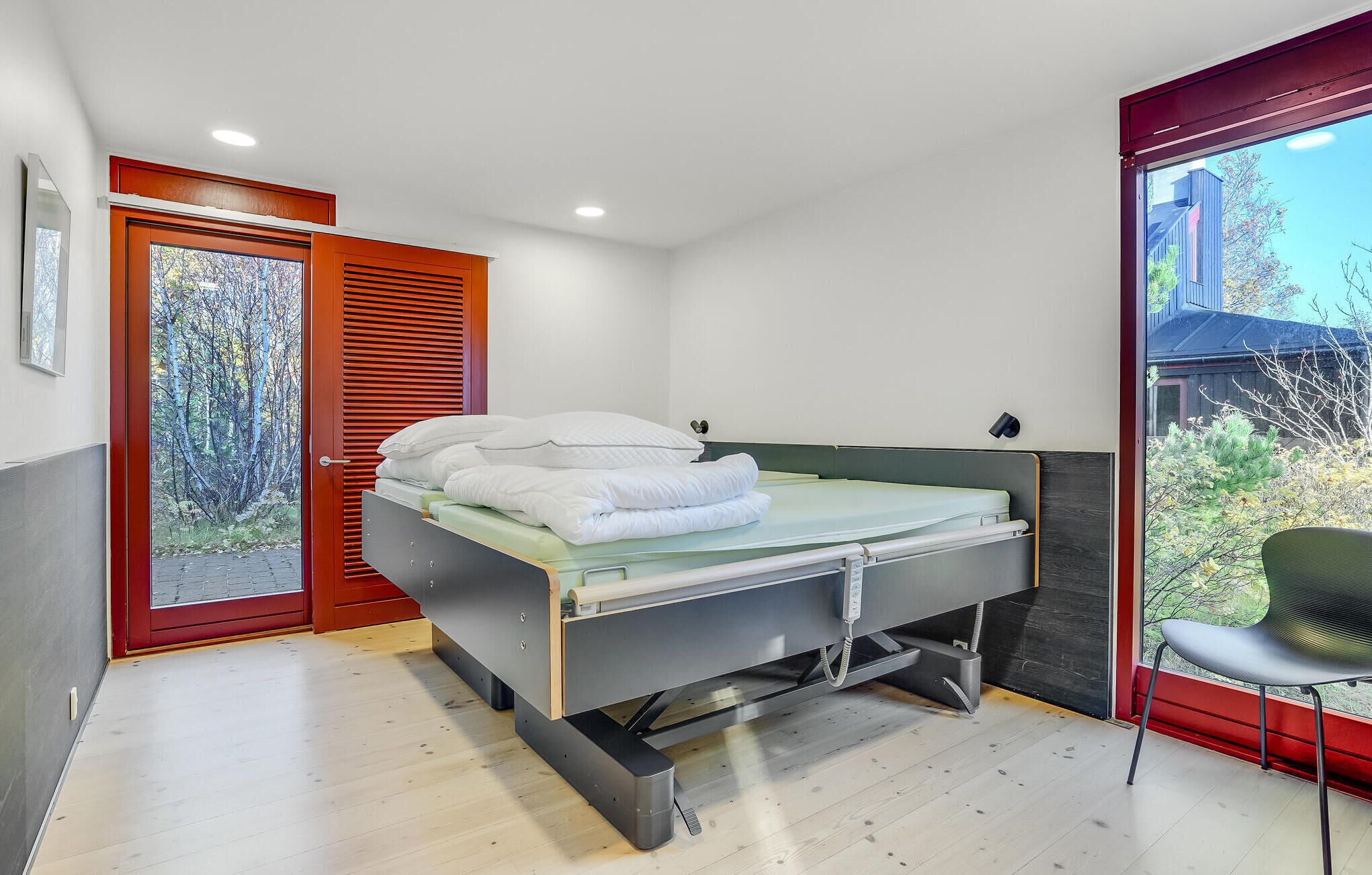 A compact bedroom with a bed, a small bedside table, a chair, and a window with a view of trees.