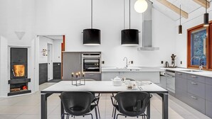 Una cucina moderna con isola centrale, due sedie nere, lampade a sospensione e forno integrato.