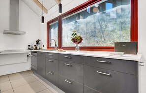 Una cocina moderna con un amplio ventanal, armarios grises y una cafetera sobre la encimera.