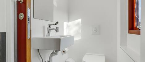Une salle de bain avec un lavabo blanc, des toilettes et une fenêtre avec des rideaux.