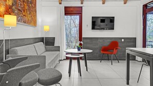 A modern living room with a grey sofa, a red chair, a small round table, and a TV mounted on the wall. - Gorgeous home in Grenaa with WiFi (Grenaa)