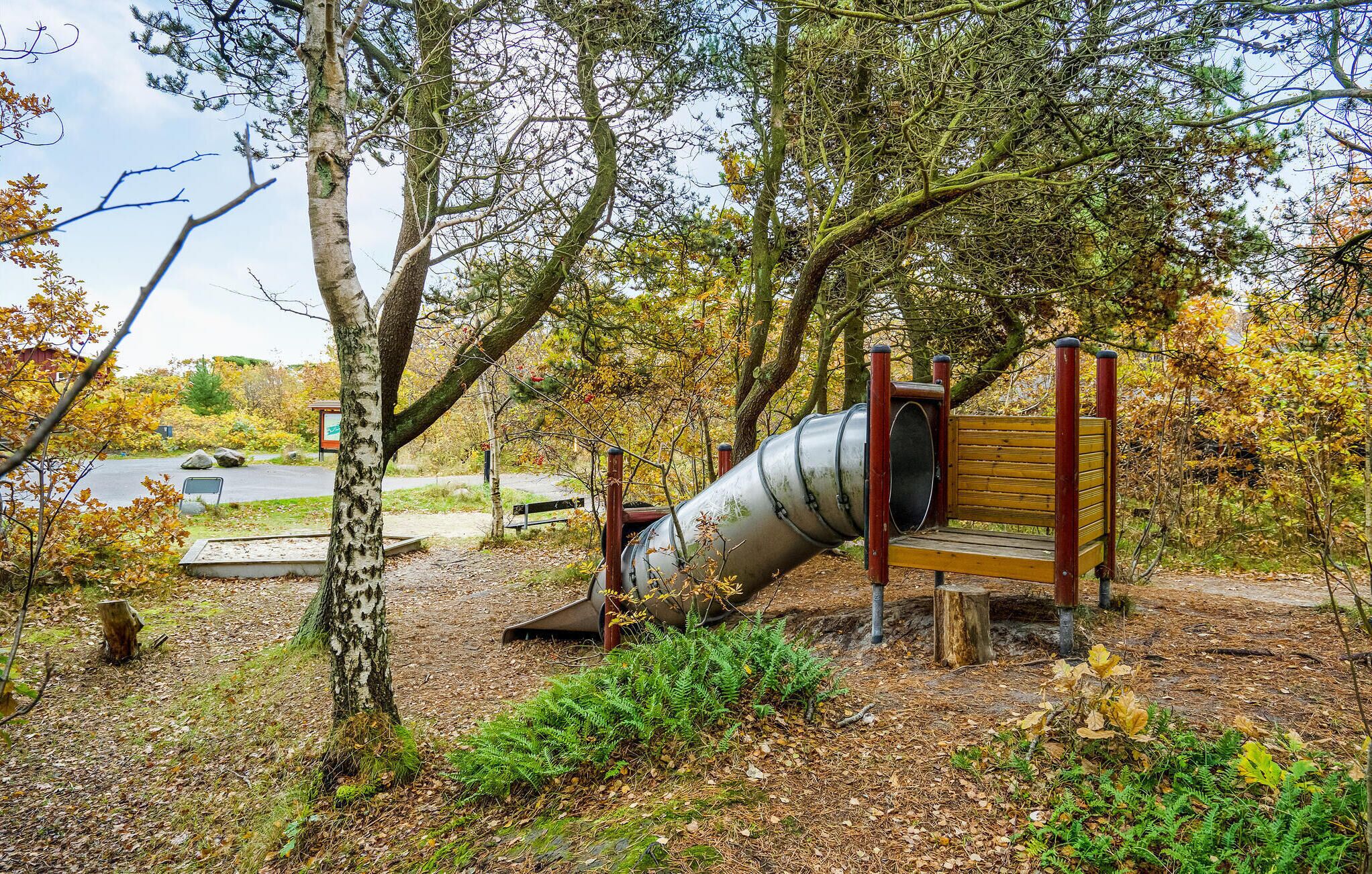 A playground with a slide and a bench, surrounded by trees and a road in the background.