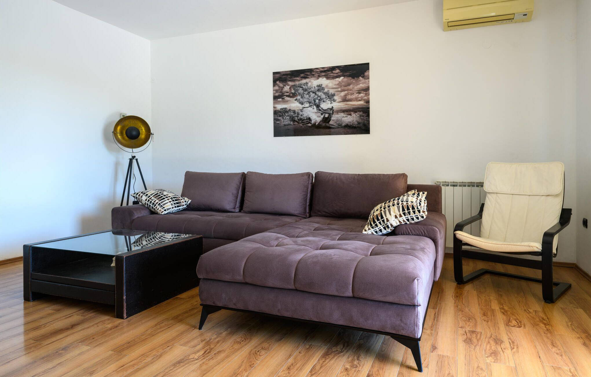 Ein modernes Wohnzimmer mit Ecksofa, Glastisch, Stehlampe und einem Sessel.