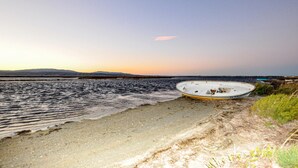 Ein Boot an einem sandigen Strand mit Wasser und Hügeln im Hintergrund.