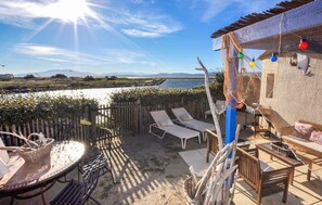 A patio with a view of a body of water, wooden furniture, and a pergola with string lights. - Pet friendly home in Le Barcarès (Le Barcarès)
