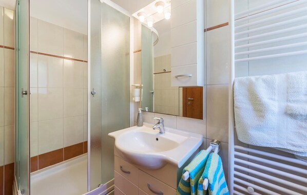 A bathroom with a glass shower enclosure, a white sink with a mirror above it, and a towel rack with a striped towel.