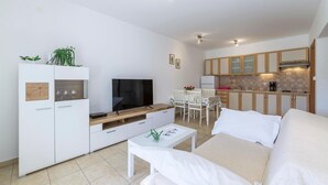 Ein modernes Wohnzimmer mit einem Flachbildfernseher, einem weißen Sofa, einem Couchtisch und einem Essbereich mit Tisch und Stühlen.