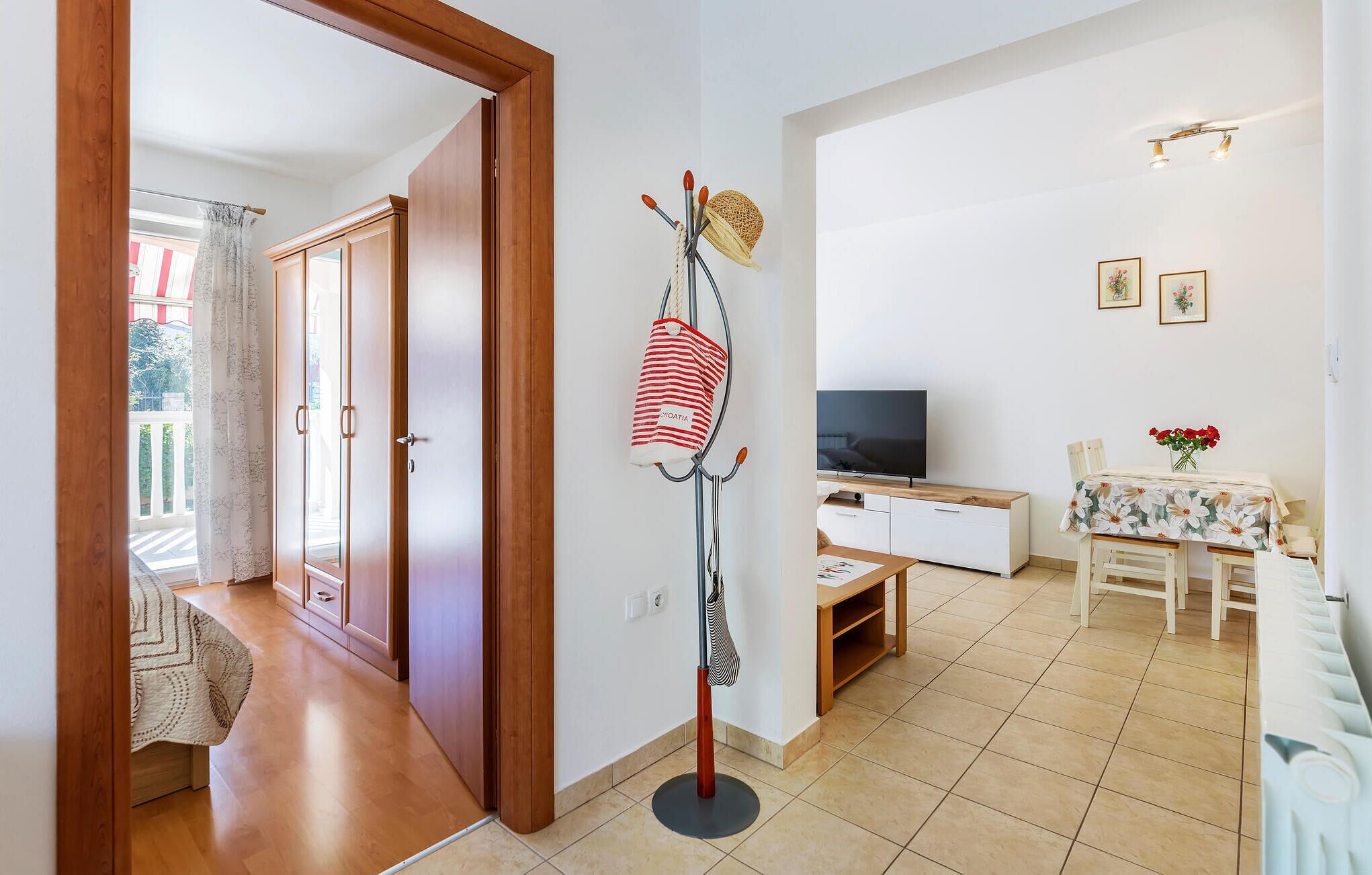 Uma sala de estar com televisão, uma mesa de jantar com cadeiras e um corredor com portas de madeira.