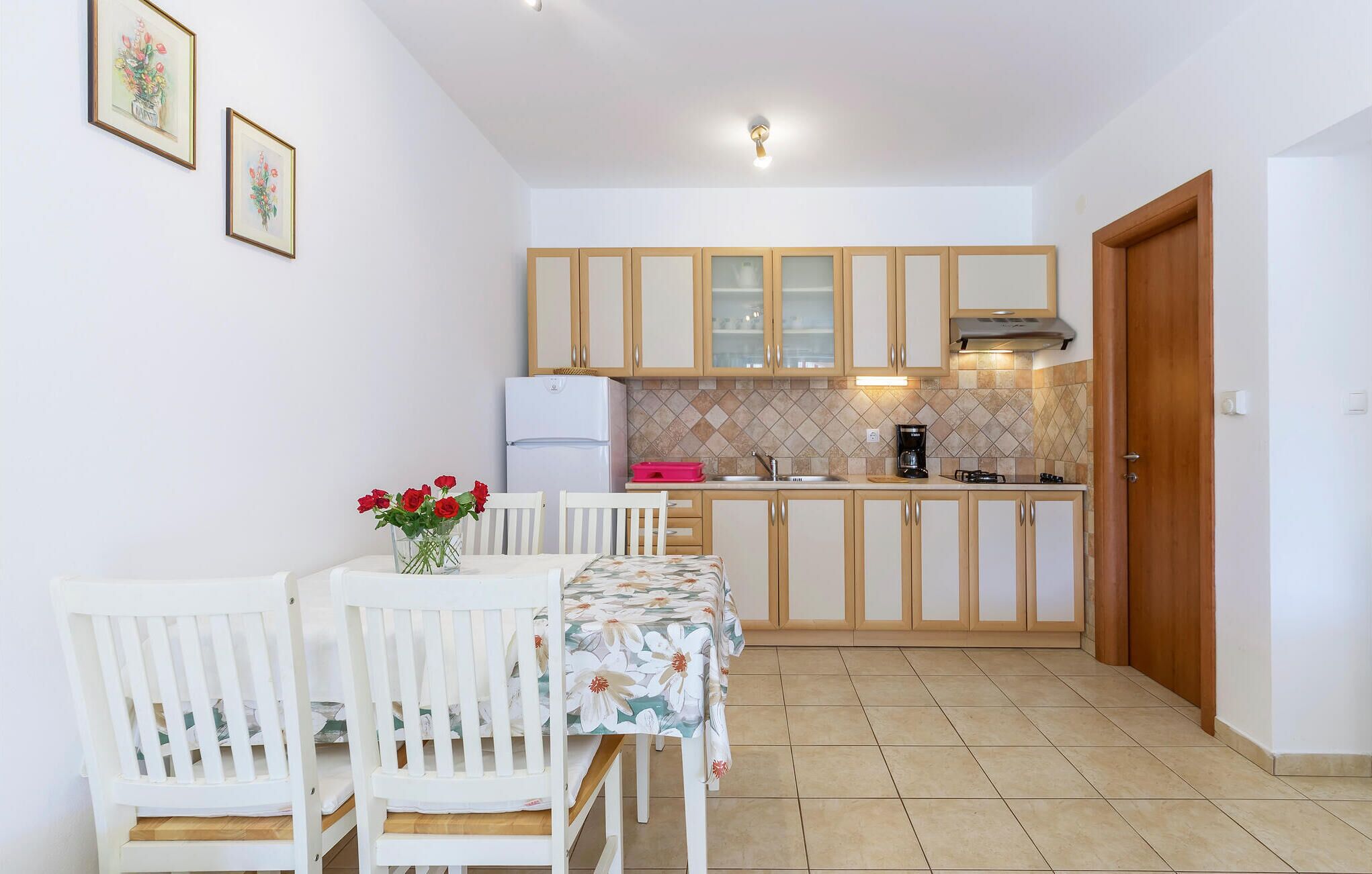 A compact kitchen with wooden cabinets, a white refrigerator, a coffee maker, and a dining table with chairs.