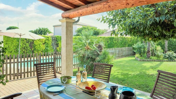 Zona pranzo all'aperto con tavolo imbandito per due, circondata da un recinto in legno e vegetazione lussureggiante.