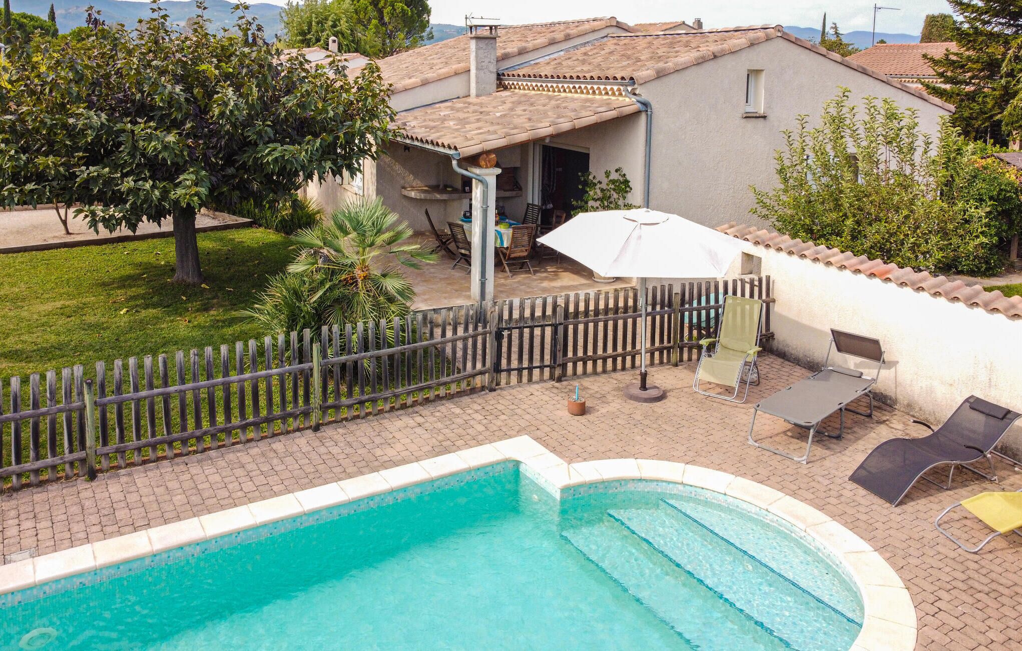 Una piscina con muelle de madera, un patio con mobiliario exterior y vista a una casa con tejado de tejas.