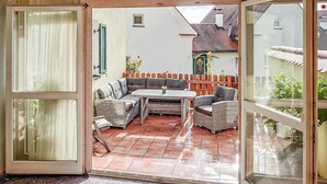 Un patio abierto con un área de descanso con cojines, una pequeña mesa y una cerca de madera.