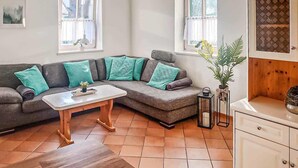Una sala de estar acogedora con un sofá gris decorado con cojines azul verdosos, una mesa de centro de madera y una pequeña planta.