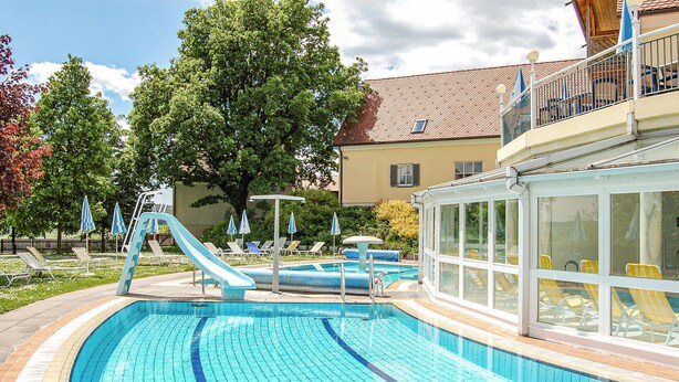 Una piscina con tobogán, tumbonas y un área acristalada con sillas amarillas.