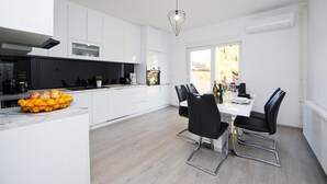 A modern kitchen with white cabinets, a dining area with a white table and black chairs, and a large window providing natural light. - Cozy home in Donji Andrijevci (Donji Andrijevci)