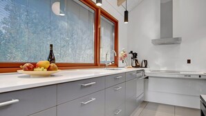 Une cuisine moderne avec des meubles gris, un plan de travail blanc, un four encastré et une fenêtre équipée de stores.