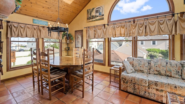 A dining area with a wooden table and chairs, a sofa, and large windows with curtains. - FABULOUS BEACH HOUSE- 7 Bedrooms,Heated Pool,12 BeachBadges,9 Car Driveway (Point Pleasant Beach)