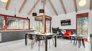 A modern kitchen with a dining area, large windows, and a TV.