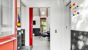 A modern hallway with a red accent wall, a dining area with a round table and chairs, and a view of the outdoors.