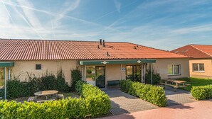 A building with a tiled roof, a covered entrance, and a patio area with benches and greenery. - 4 bedroom gorgeous home in Den Ham (Den Ham)