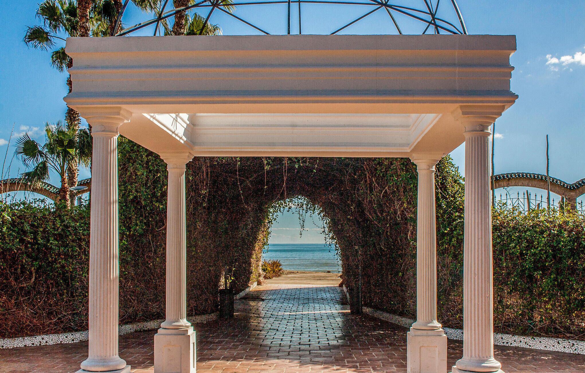 Une allée couverte, bordée de colonnes, qui mène à la plage.