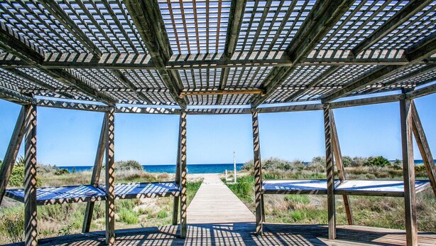 A wooden deck with a grid-like ceiling structure, leading to a beach. - 2 bedroom beach front apartment in Cabanes (Cabanes)