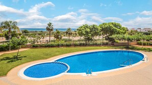 A large, oval-shaped swimming pool with a clear blue water, surrounded by a well-maintained lawn and palm trees. - 2 bedroom beach front apartment in Cabanes (Cabanes)