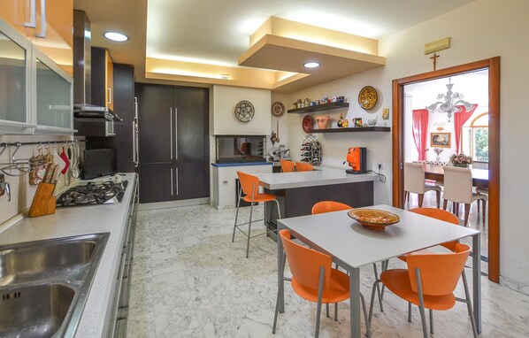 Une cuisine moderne avec un coin repas, dotée d’un sol en marbre, de chaises orange et d’une table blanche.