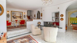 Un amplio salón con suelo de mármol, muebles rojos y dorados, una chimenea y un cuadro grande.