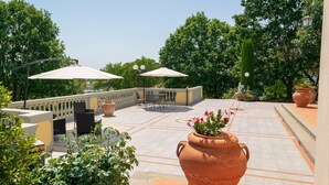 Un patio al aire libre con una mesa y sillas, rodeado de macetas de terracota grandes y plantas en macetas.