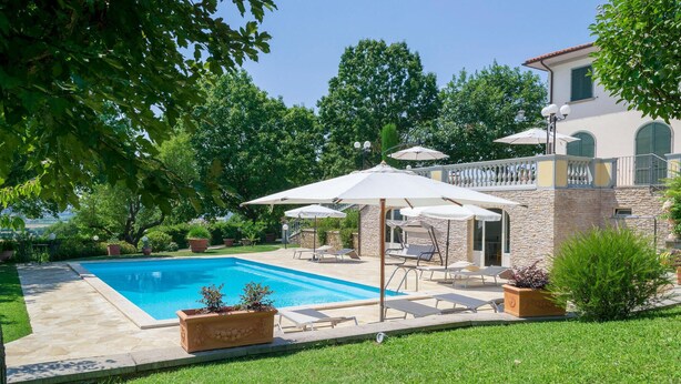 Un patio trasero con piscina, mobiliario exterior y un edificio de piedra.