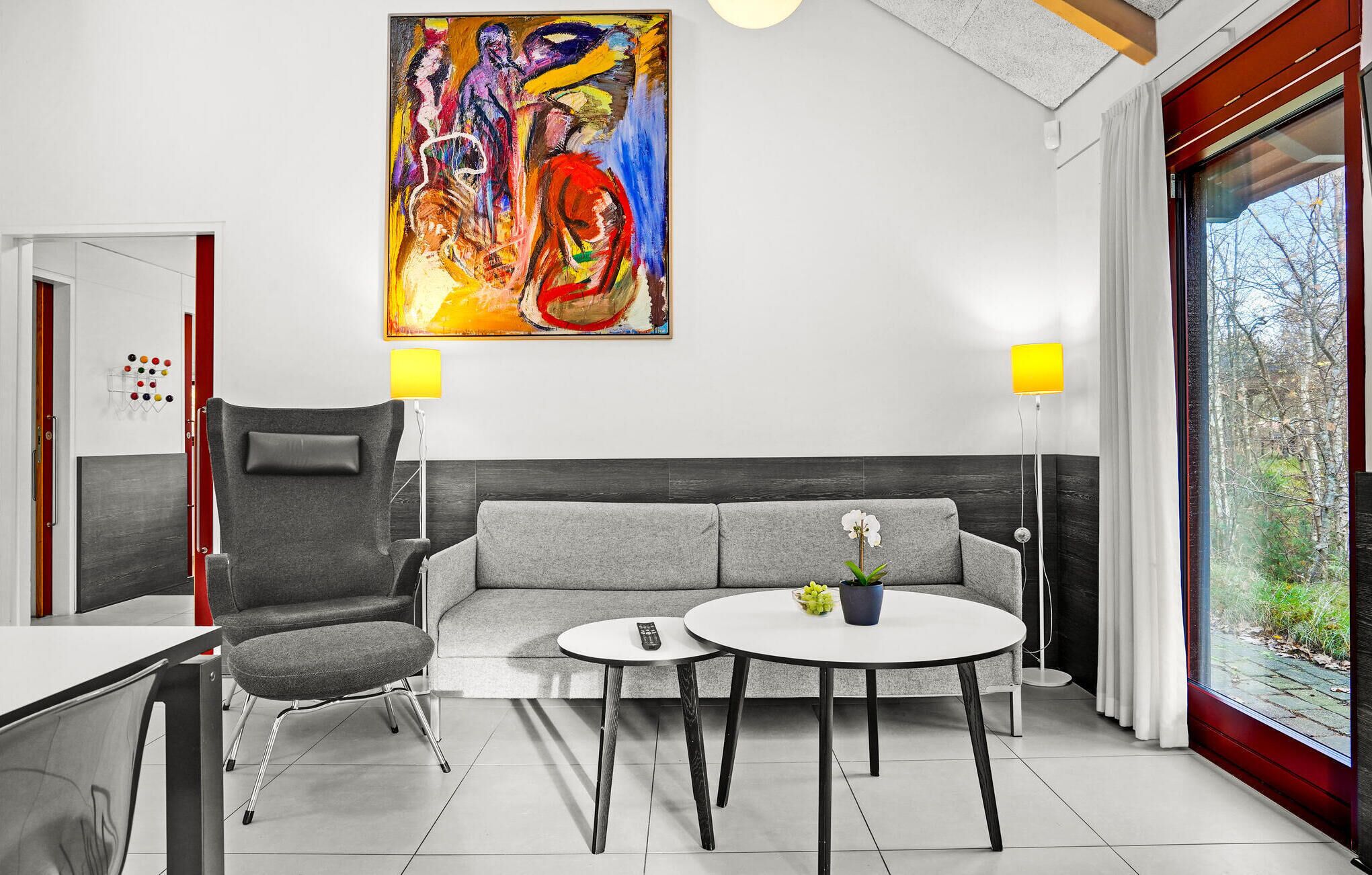 A modern living room with a grey sofa, a round coffee table, a grey armchair, and a painting on the wall.