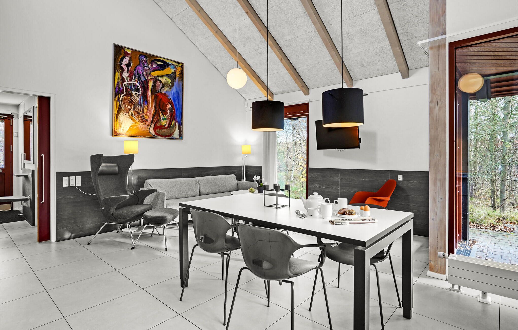 Zona pranzo moderna con tavolo bianco, sedie grigie e un quadro astratto dai colori vivaci appeso alla parete.