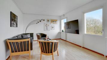 Un salon spacieux doté d’une grande fenêtre, d’un canapé, de deux fauteuils, d’une petite table et de plusieurs œuvres d’art encadrées accrochées aux murs.